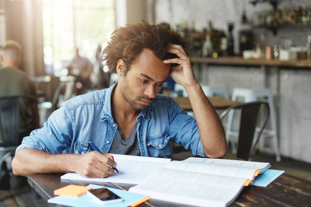 Indoor shot of focused handsome stylish black European university student having serious concentrated face expression while learning lesson at cafe in the morning, solving mathematical problems