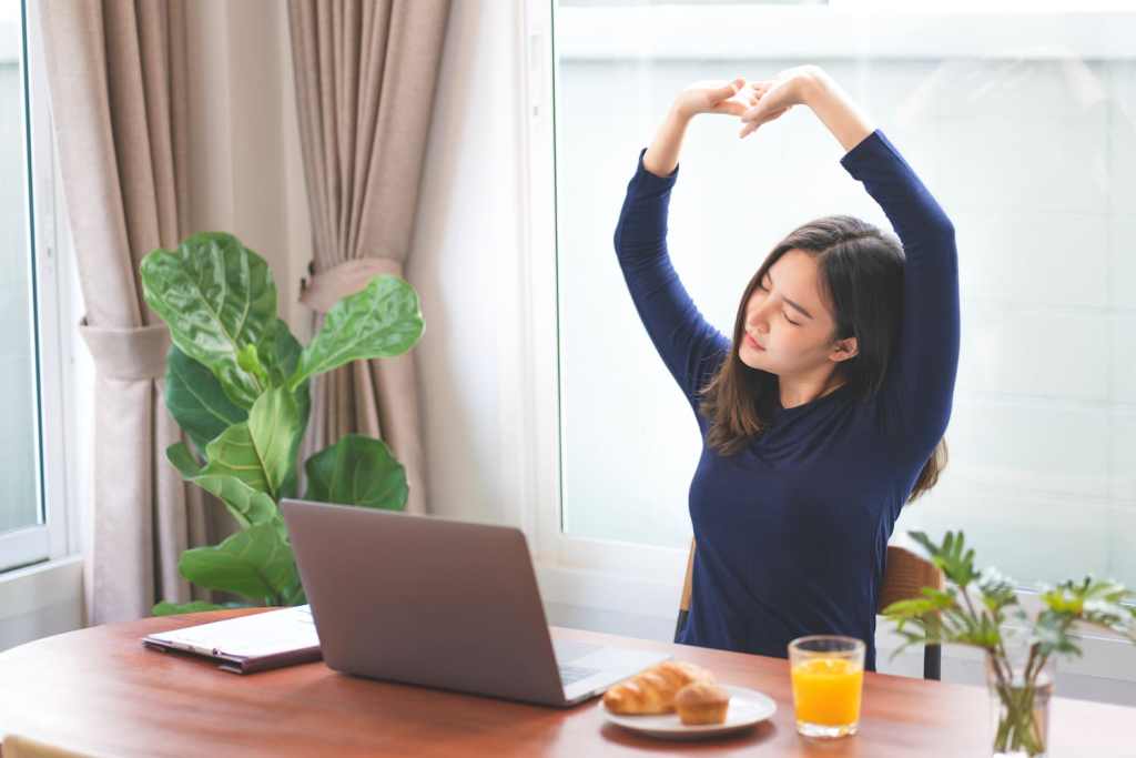 Young asian woman stretching relaxation resting office behind her desk working productive