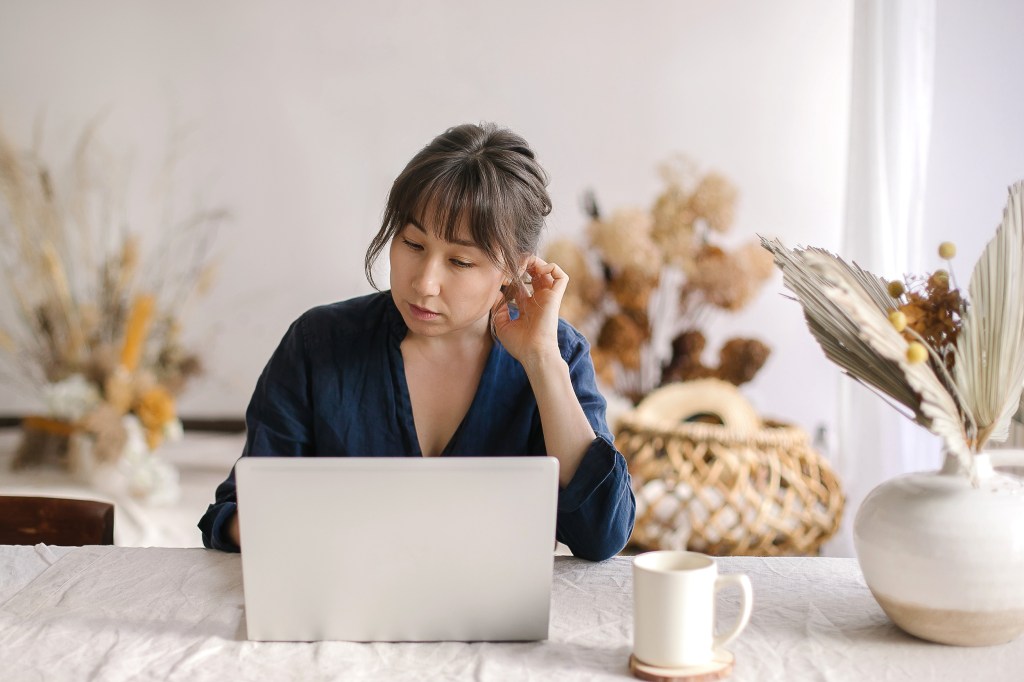 Busy focused asian woman freelancer working remotely on laptop computer at cozy home office, business woman sitting at table and looking at pc screen. Freelance, remotely work concept