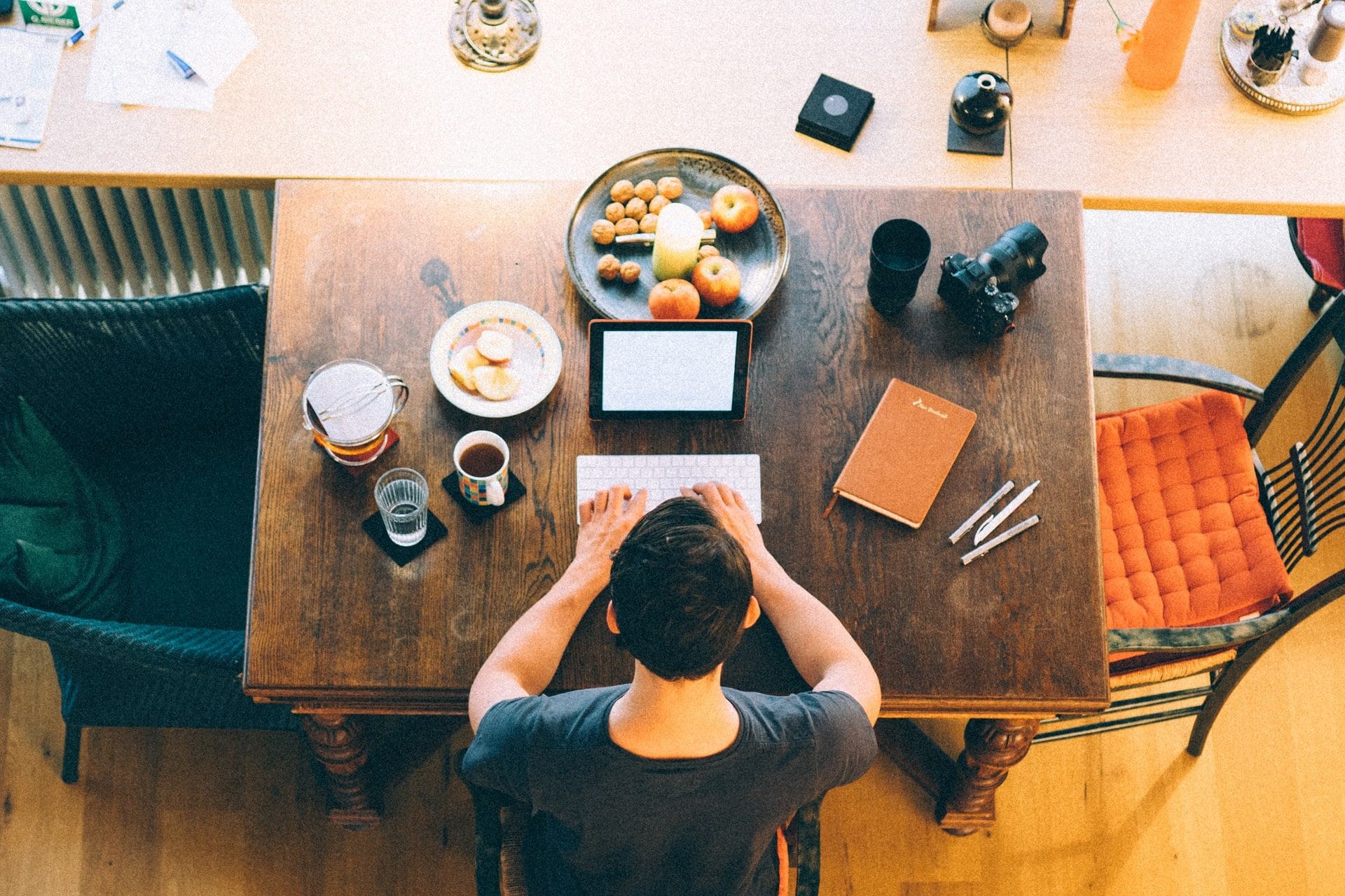 A man sitting at table with breakfast, his laptop, and a journal and pens