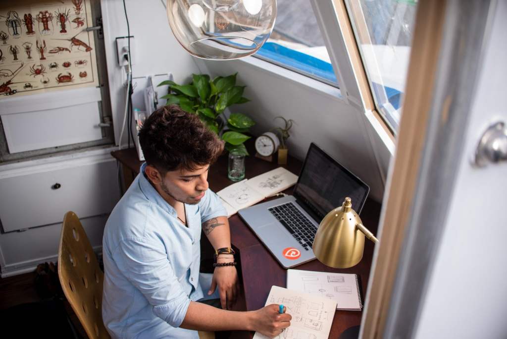 man sits at home working on his computer and sketching