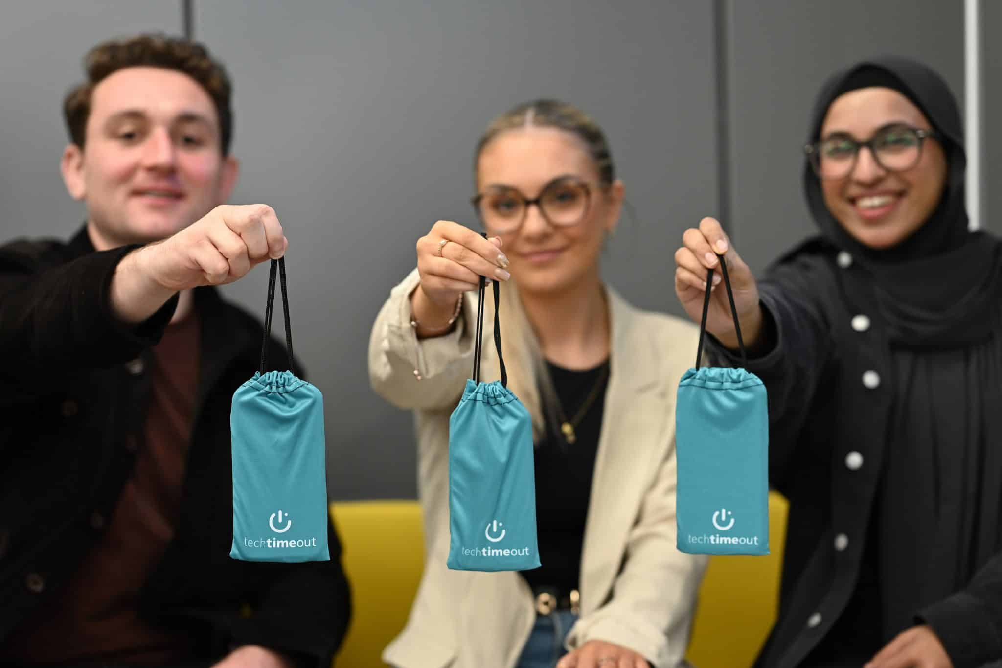 Three people holding tech devices and a pouch labeled "Tech Timeout."