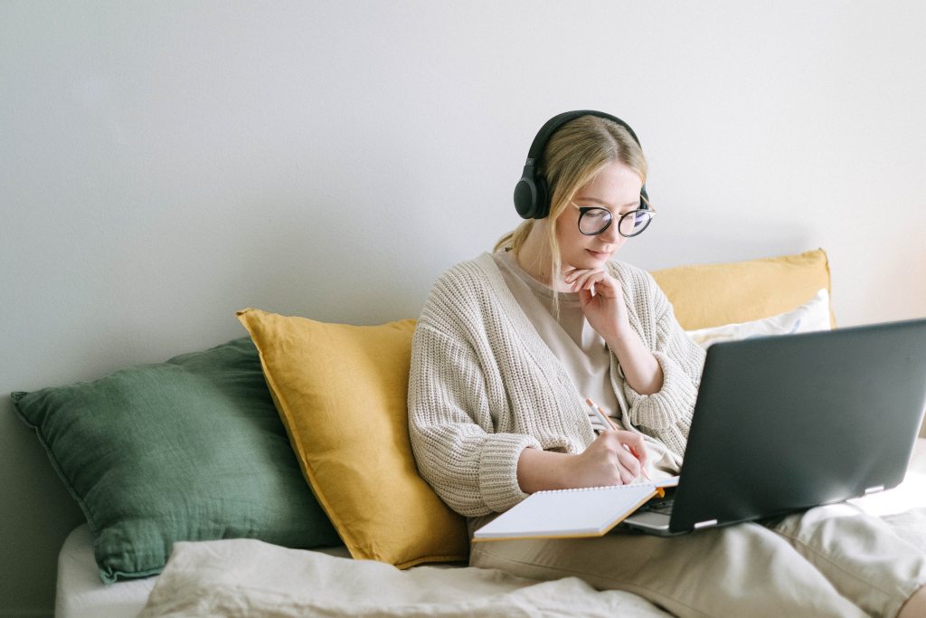 Teen girl studies with headphones, laptop and notepad