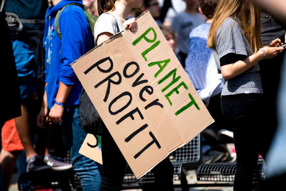 A person protesting against consumerism, holding a sign that reads "Planet Over Profit."