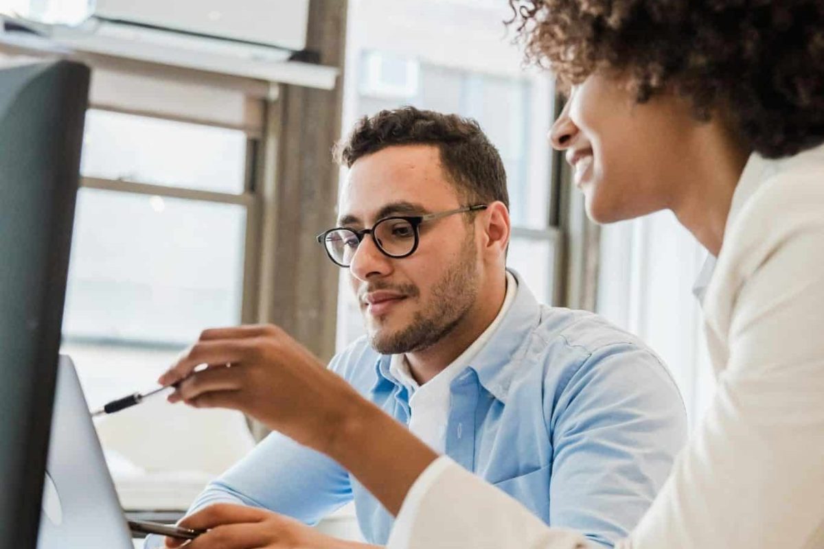 A woman explains something to a man on a laptop. They appear to be engaged in a coaching session.