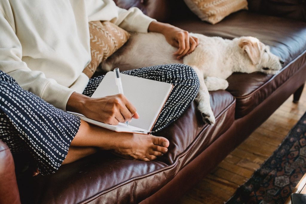 woman taking notes on couch while dog relaxes beside her