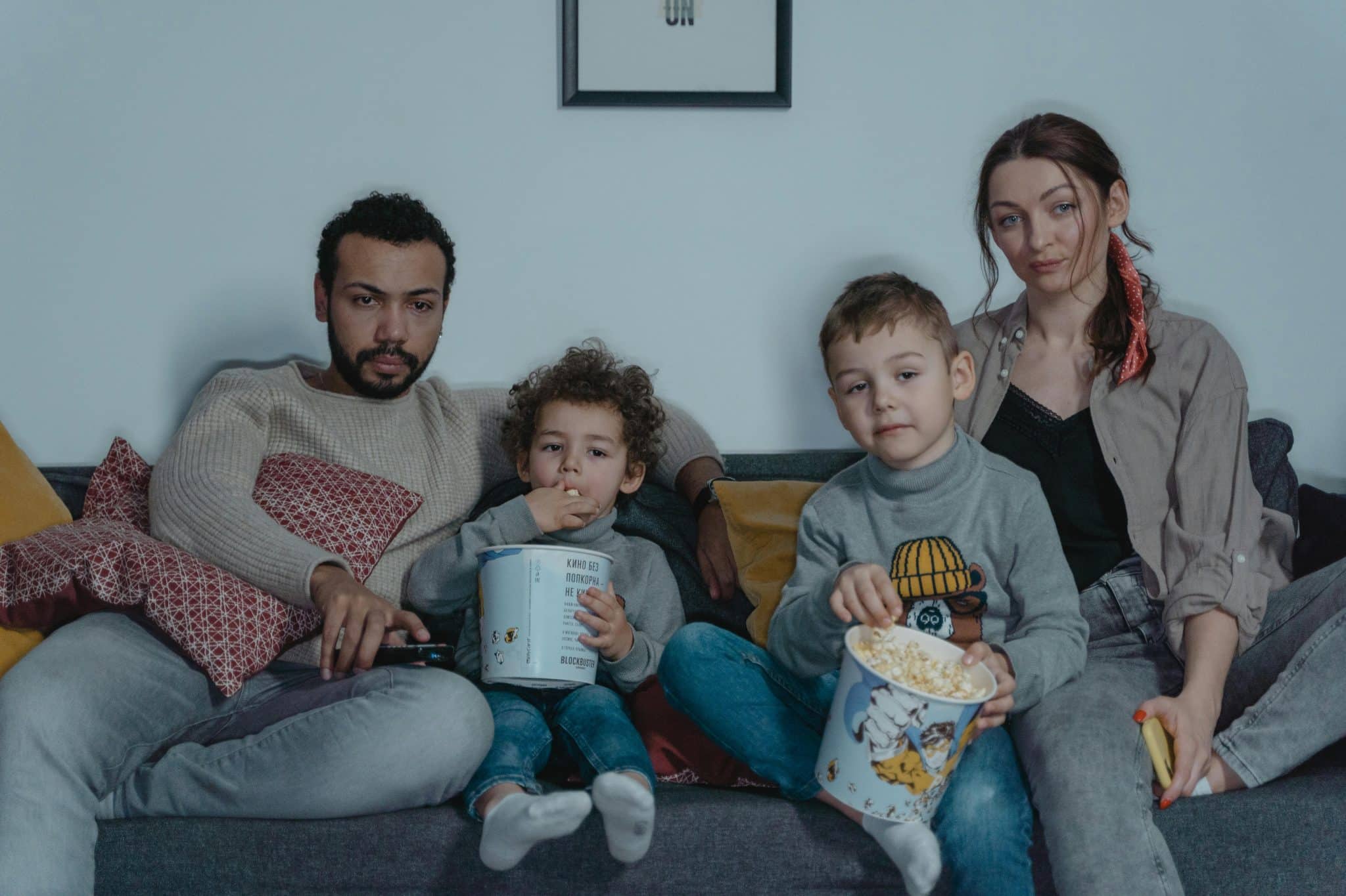 A family of four, two parents and two children, sitting together on a couch watching television.