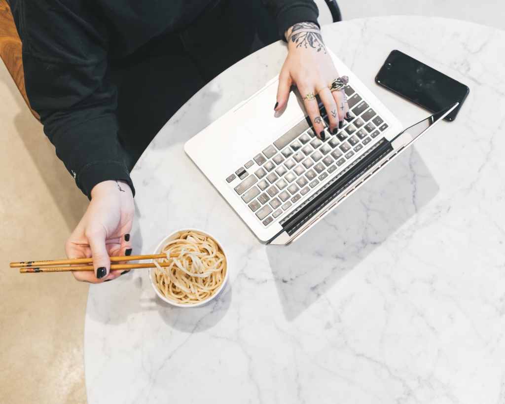 Woman sitting at computer multitasking by eating food